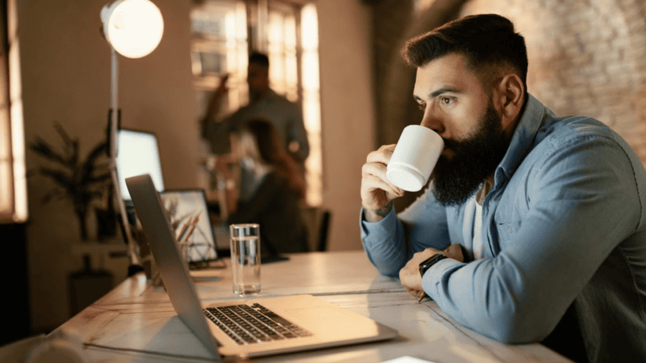 Muž v práci za stolem popíjející kávu