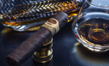 Luxusní doutník značky Padron opřený o zlatý zapalovač, v pozadí elegantní karafa a sklenka s tmavým destilátem – stylová atmosféra, která podtrhuje noblesu a tradici světa prémiových doutníků