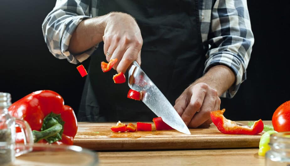 Ruce člověka krájejí rajčata ostrým kuchyňským nožem na dřevěném prkénku - ilustrační obrázek k článku, jak vybrat kuchyňský nůž na Trendymagazin.cz
